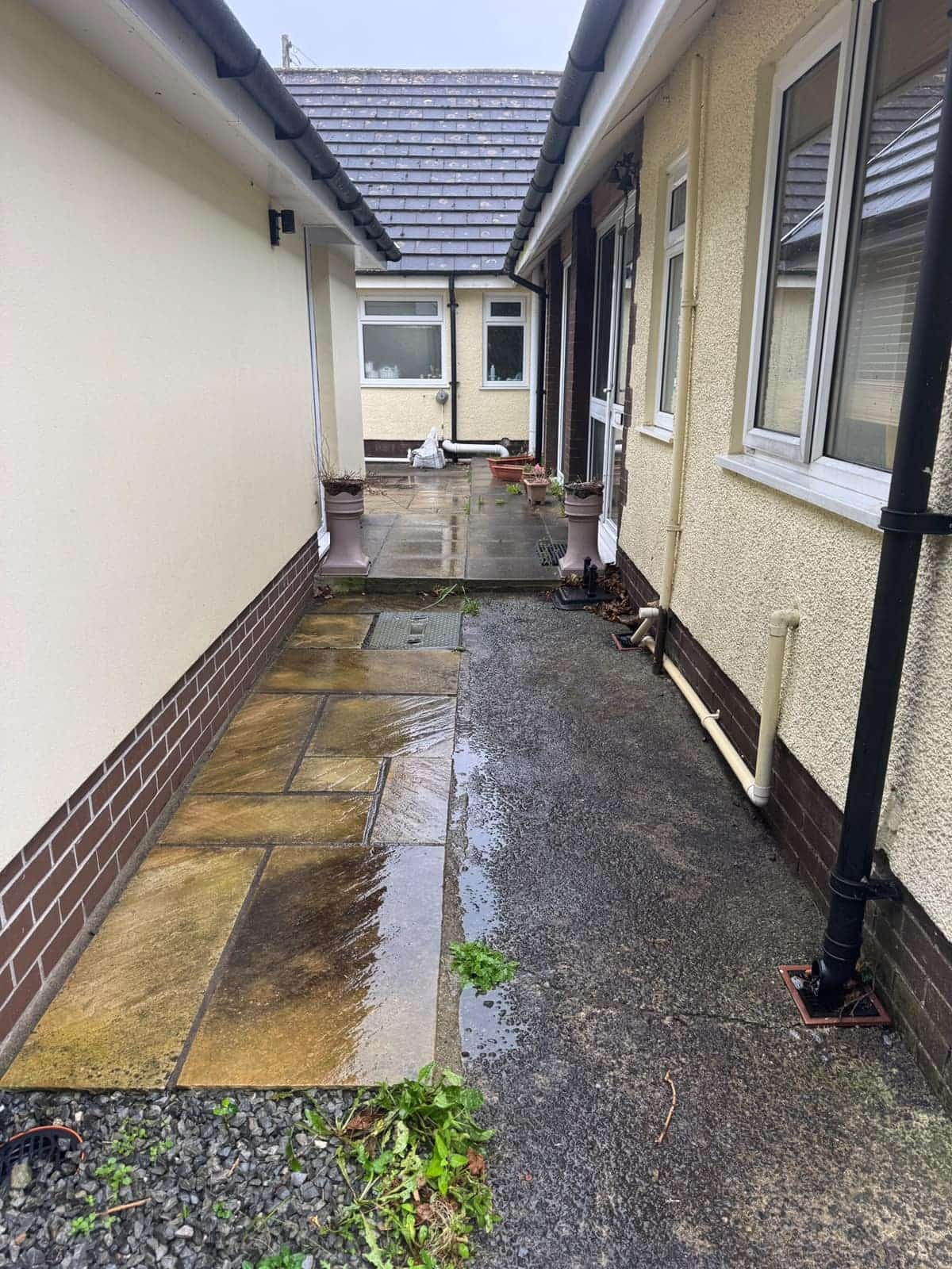 Narrow sandstone path down the side of a bungalow before cleaning, grimy with weeds at the edges