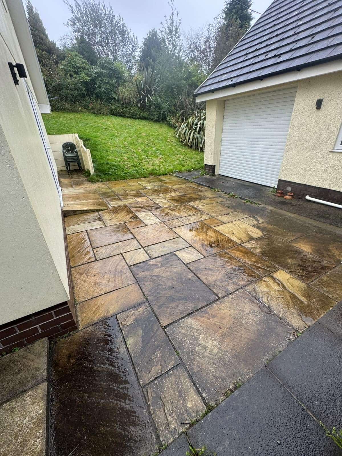 Sandstone patio beside a garage before cleaning, the slabs dark and dirty
