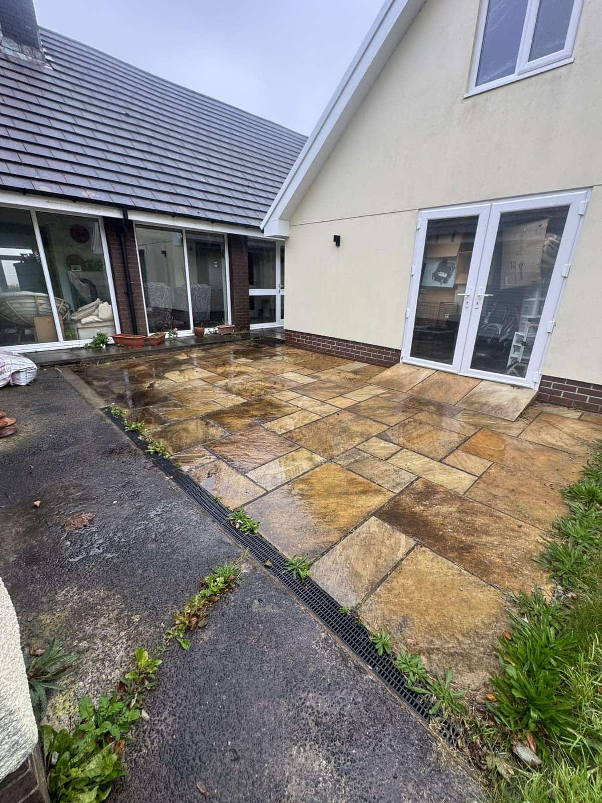 Sandstone patio outside a set of French doors before cleaning, dark with dirt and weeds along the drain